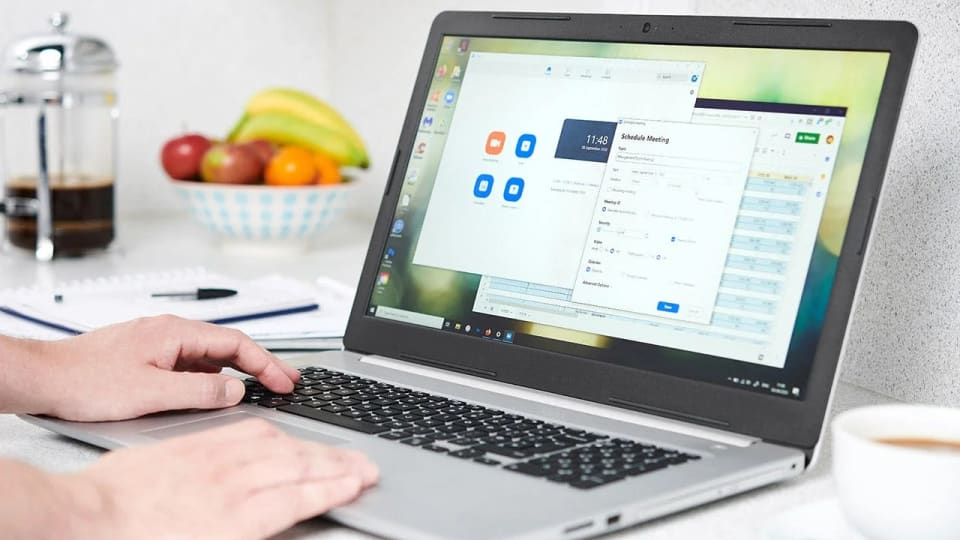 Person typing on a laptop beside a fruit bowl.