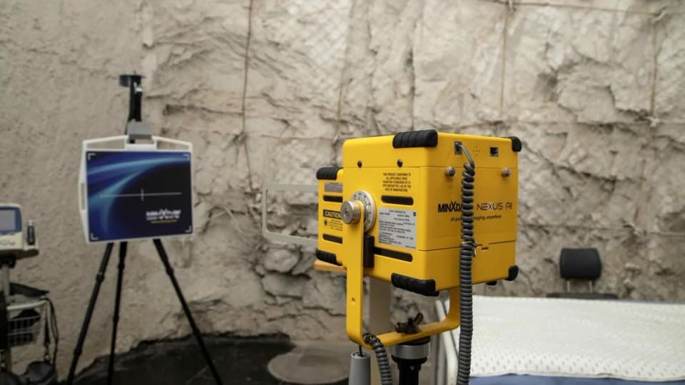 Yellow MinXray Nexus AI portable X-ray device beside a digital display and examination bed.
