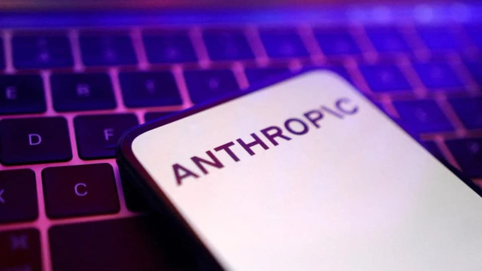 Phone displaying the Anthropic name resting on a purple-lit laptop keyboard.
